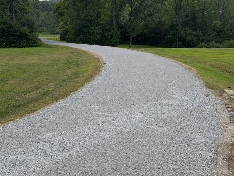 A freshly graded crushed-stone driveway curving through a tree-lined property