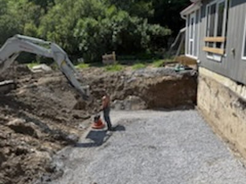 Excavated foundation area backfilled with crushed stone alongside a house