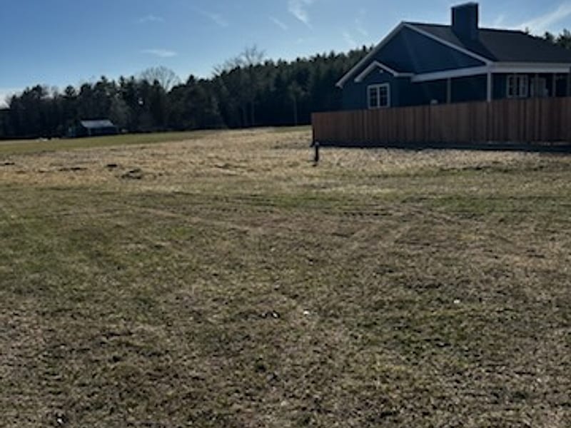 An open levelled lot beside a house with a treeline beyond