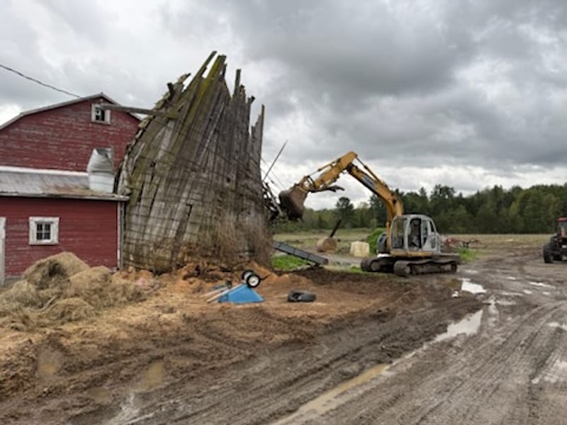 Excavator taking down an old concrete stave silo beside a red barn in Fort Ann, NY