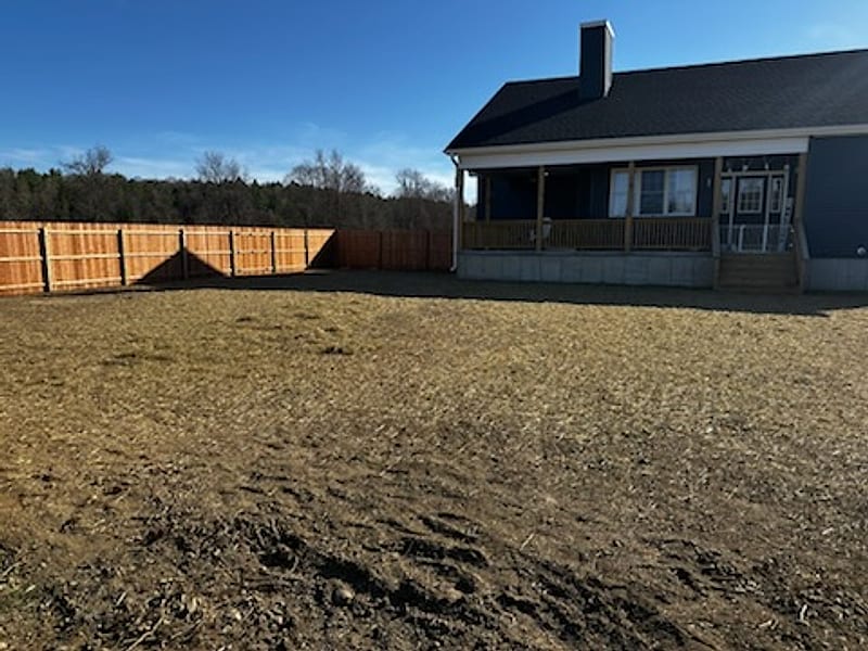 A graded back lot along a new wooden fence beside a house