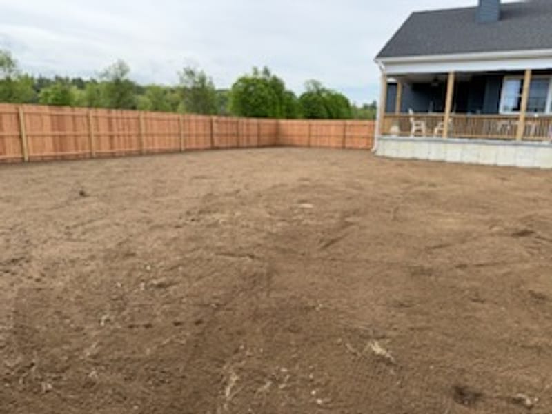 A back yard graded flat to fresh soil behind a new home, ready for seeding