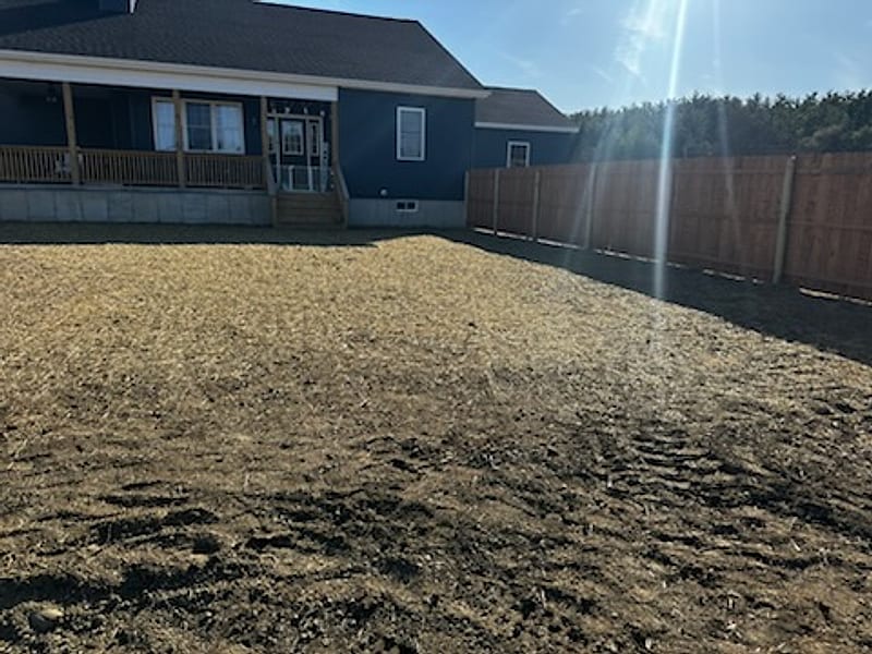 Rough-graded soil across a fenced back yard behind a blue house
